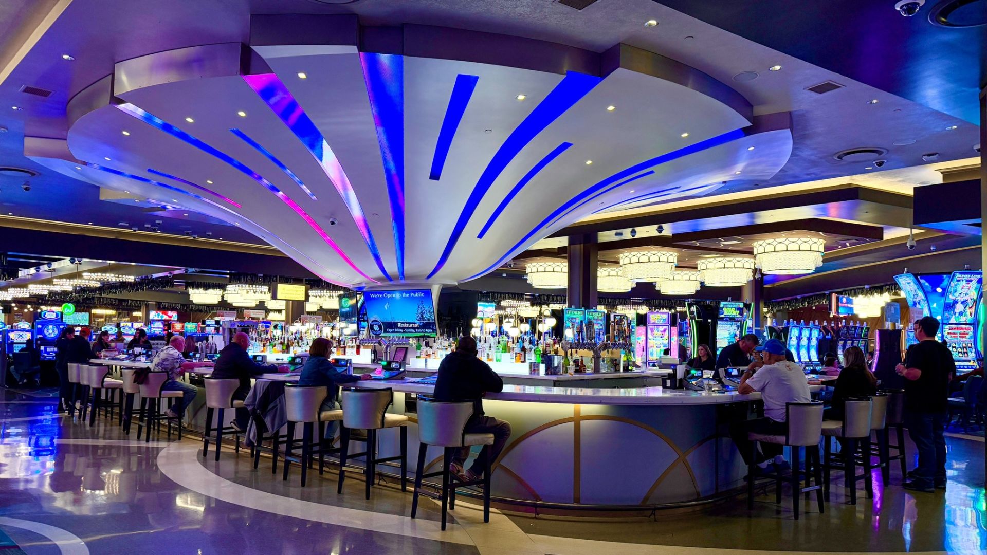 A Group Of People Sitting At Tables In A Large Room With A Large Screen And Lights